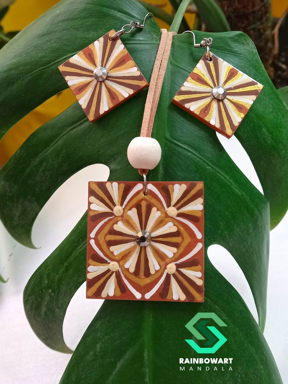 نمای نزدیک از ست گردنبند و گوشواره قهوهای کرم با نقوش دات ماندالا، تصویربرداری روی زمینه برگ طبیعی